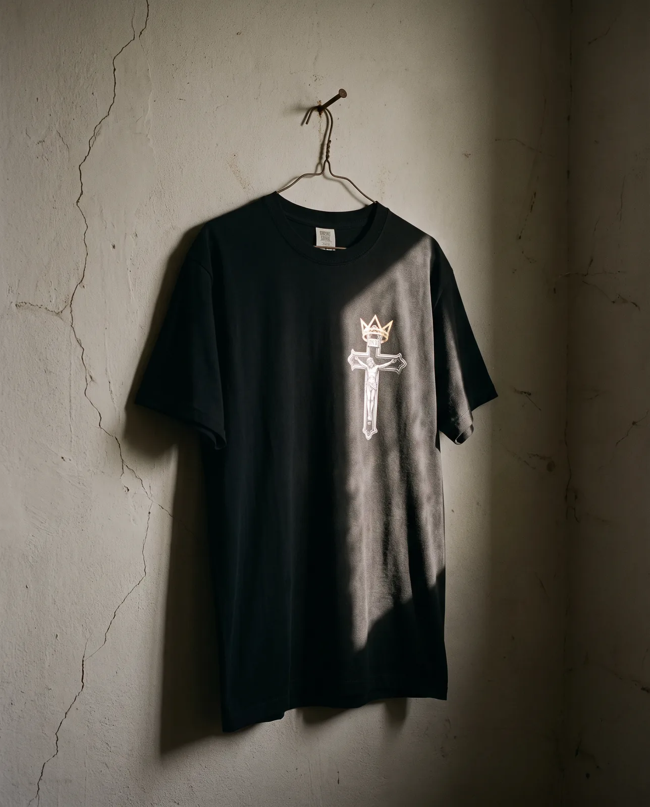 A Crowned Choices tee hanging on a bare wall in a shaft of daylight
